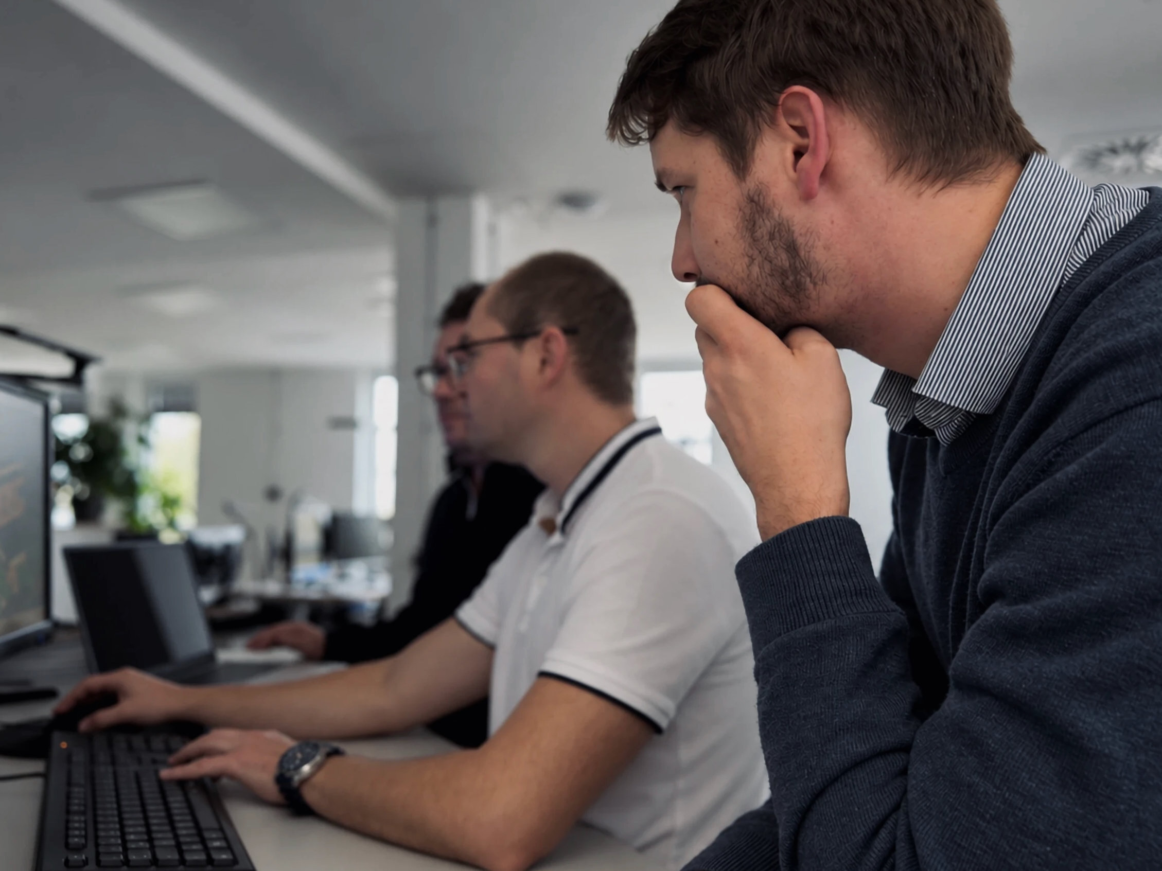 Warnow Design engineer thinking at his workstation, a colleague at a computer in the background