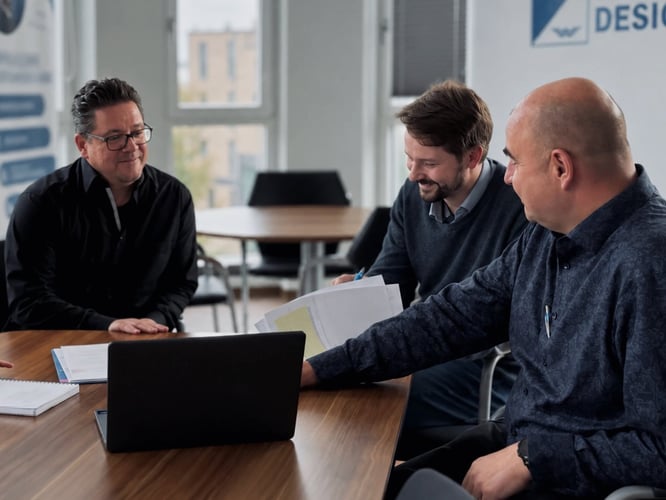 Three members of the Warnow Design team discussing documents at a meeting table