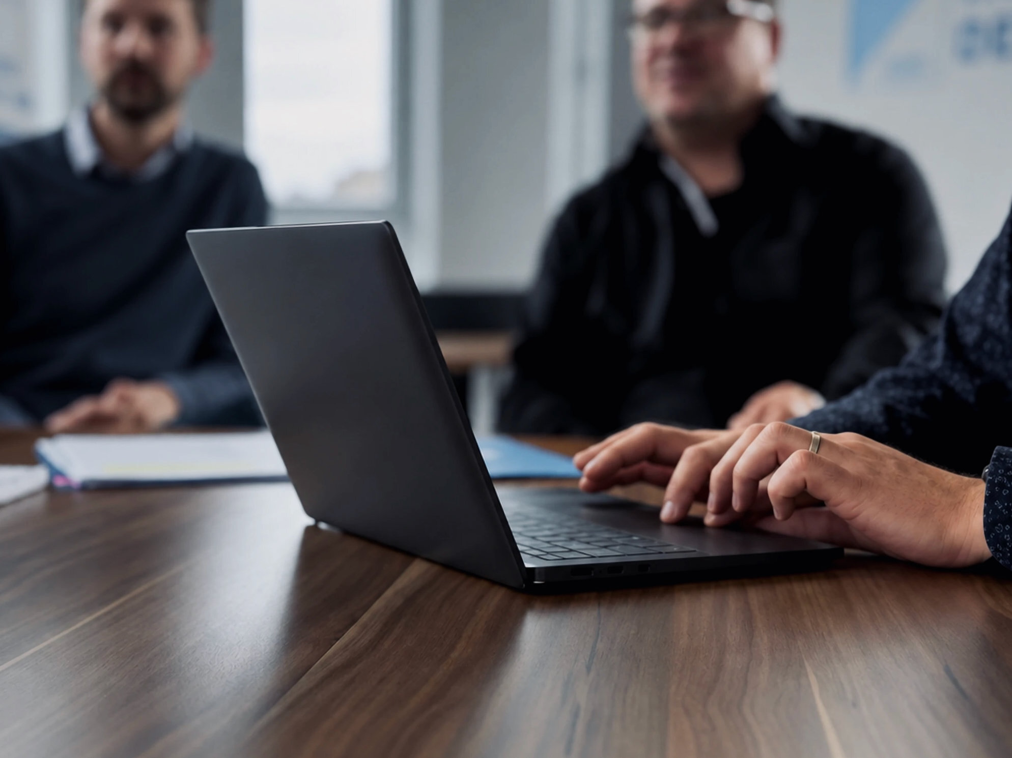 Laptop on the meeting table with Warnow Design engineers talking in the background